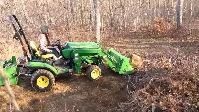 Picture of a landscape contractor on a John Deere tractor clearing rocks and tree stumps from an area to be rototilled